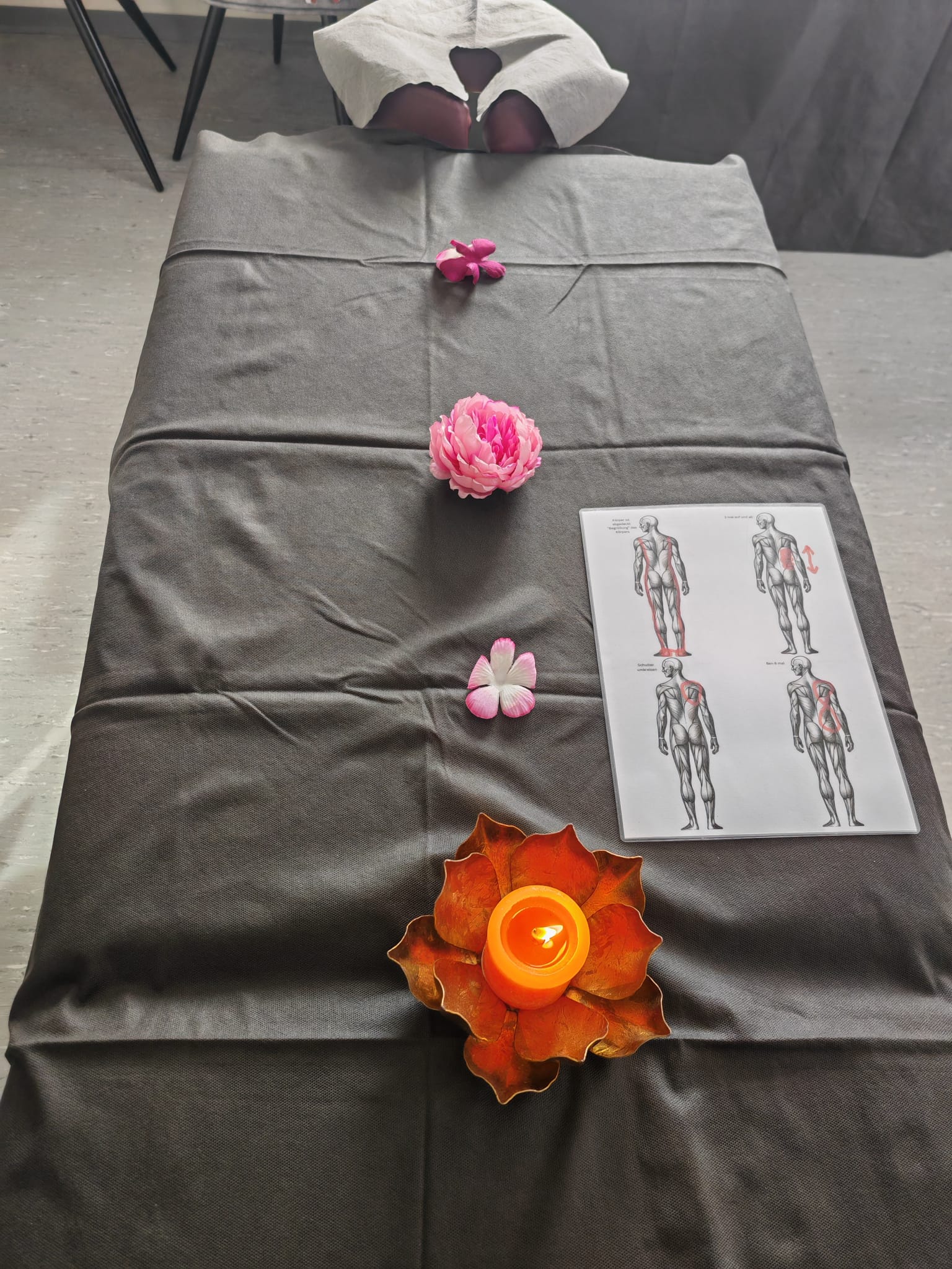 Vorbereitete Massageliege mit Blumen, Kerze und Lernunterlagen – Massageschule Baumann
